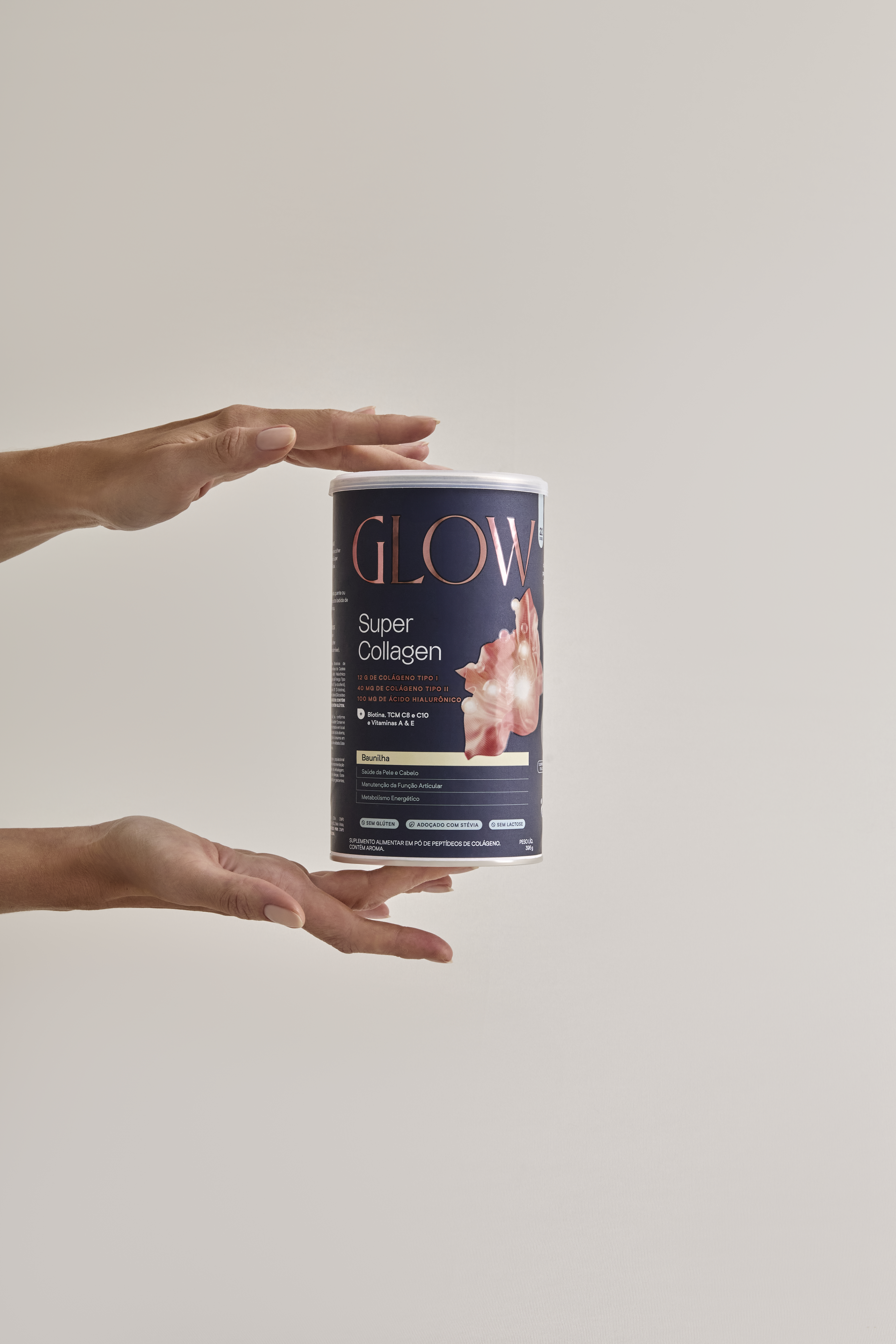 Mãos segurando o pote do suplemento Glow Super Collagen sabor Baunilha, com embalagem azul-marinho e detalhes em rosa dourado